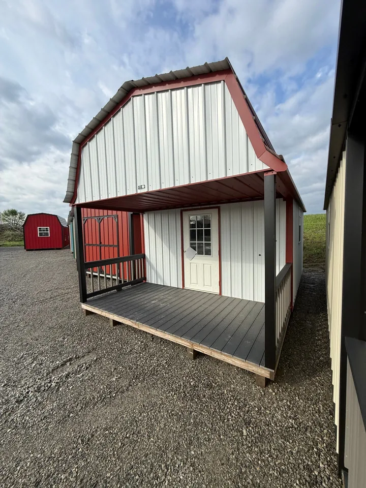 Front view of a red and white barn-style portable cabin with covered porch and dark railings