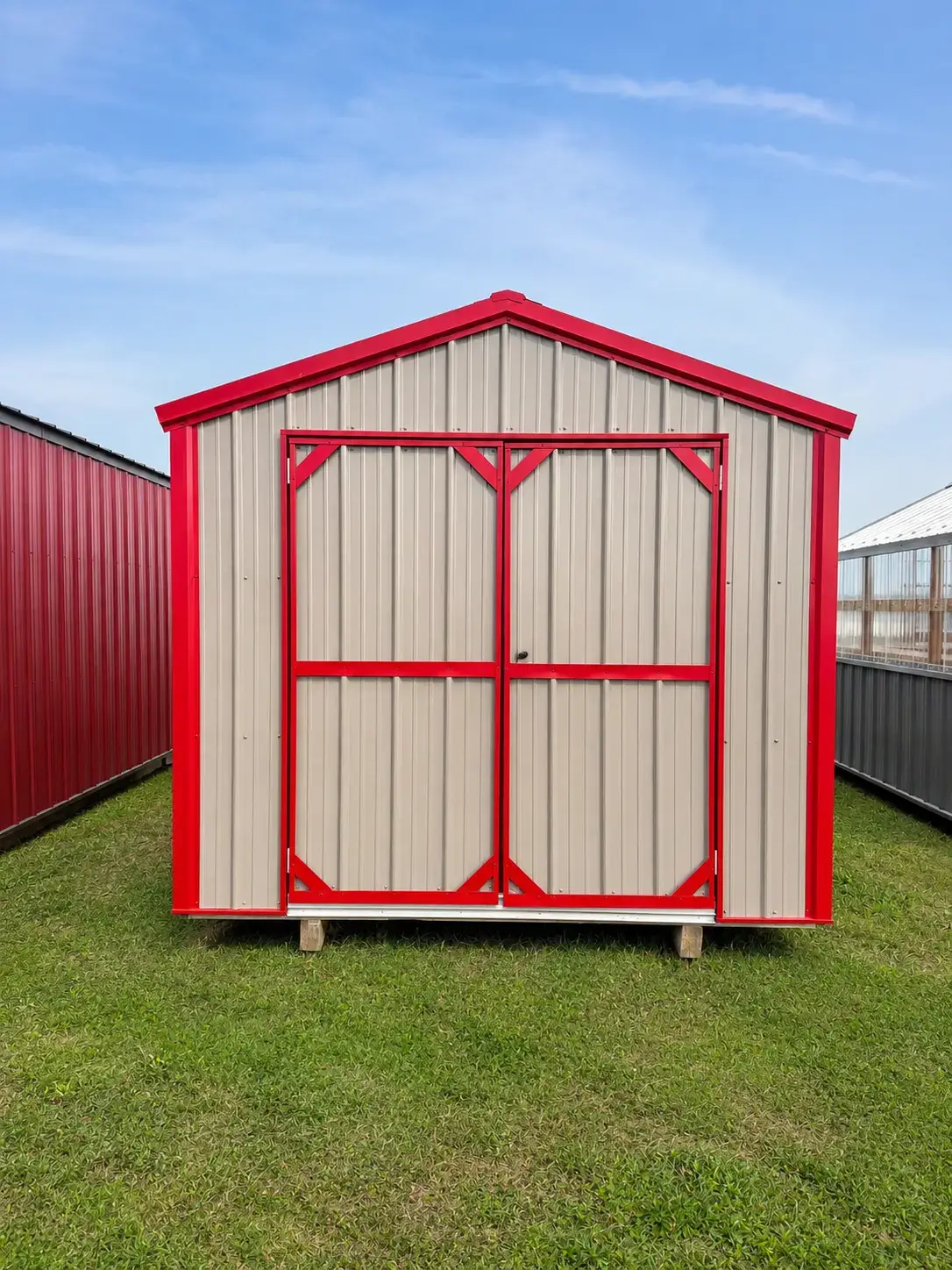 Tan metal utility shed with red trim and double doors on a Missouri lot