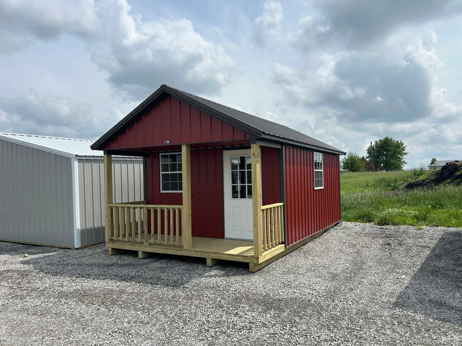 Red metal-sided portable cabin with black gable roof, covered wooden porch, and white entry door