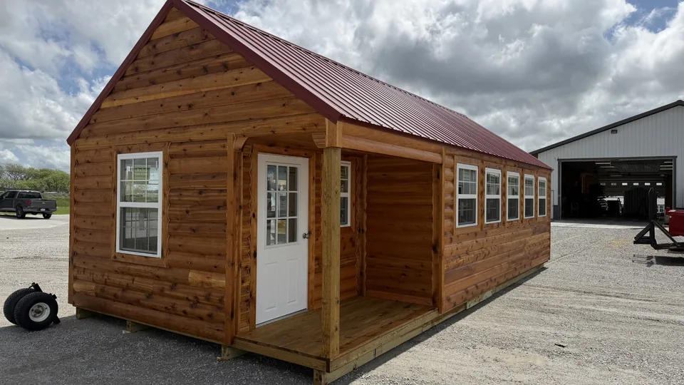 Rustic log-style cabin with red metal roof, covered porch, and multiple white-trimmed windows