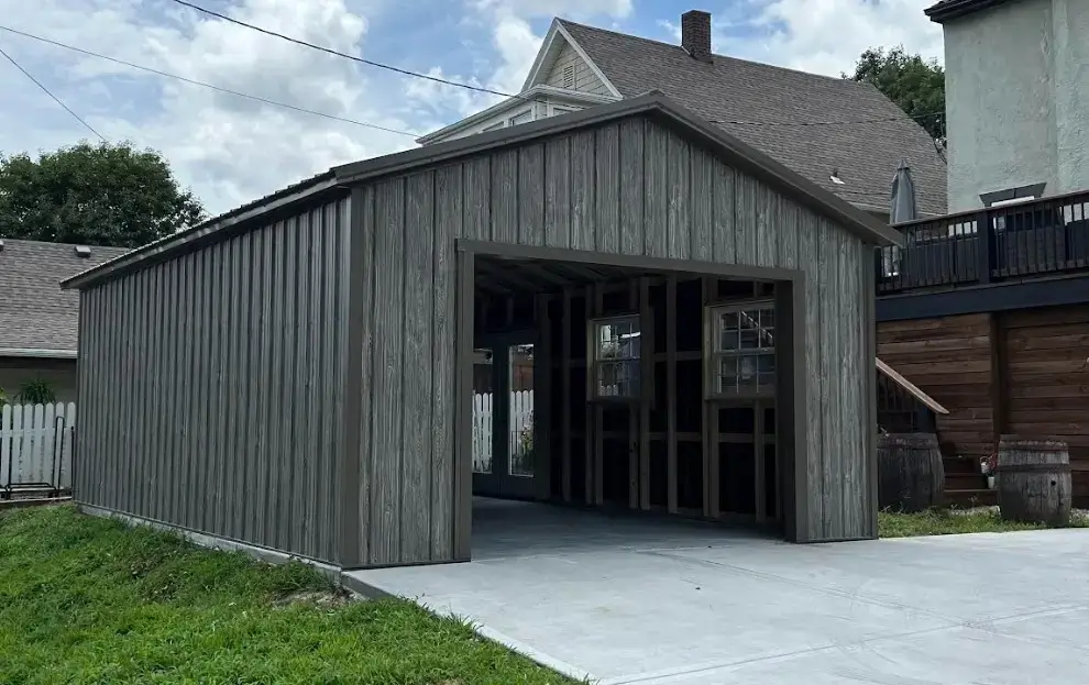 Weathered wood-look portable garage with a tall open bay beside a house