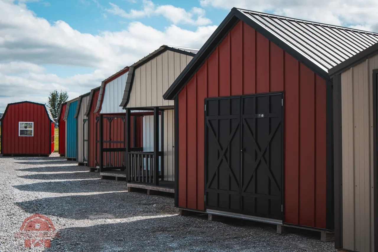 Row of red, blue and tan portable buildings on the Midwest Mini Barns lot, led by a large red storage shed with black doors