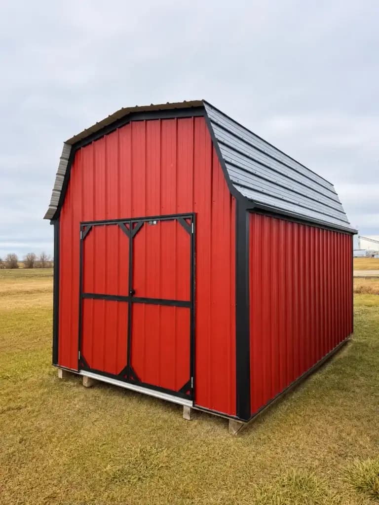 Red barn-style mini barn with black trim in an open field