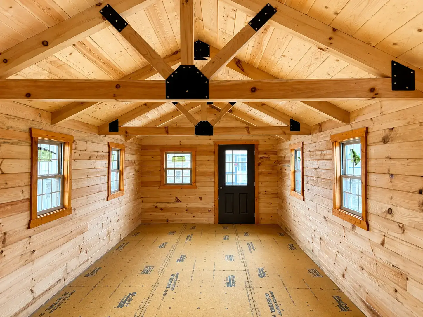 Interior of a log cabin shell with exposed timber trusses, wood walls, and windows
