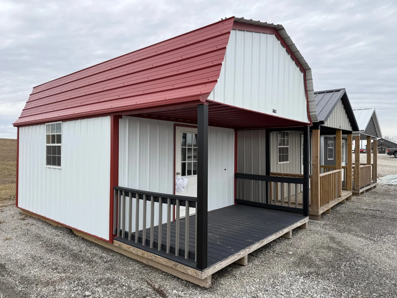 White metal barn-style cabin with red gambrel roof and covered front porch