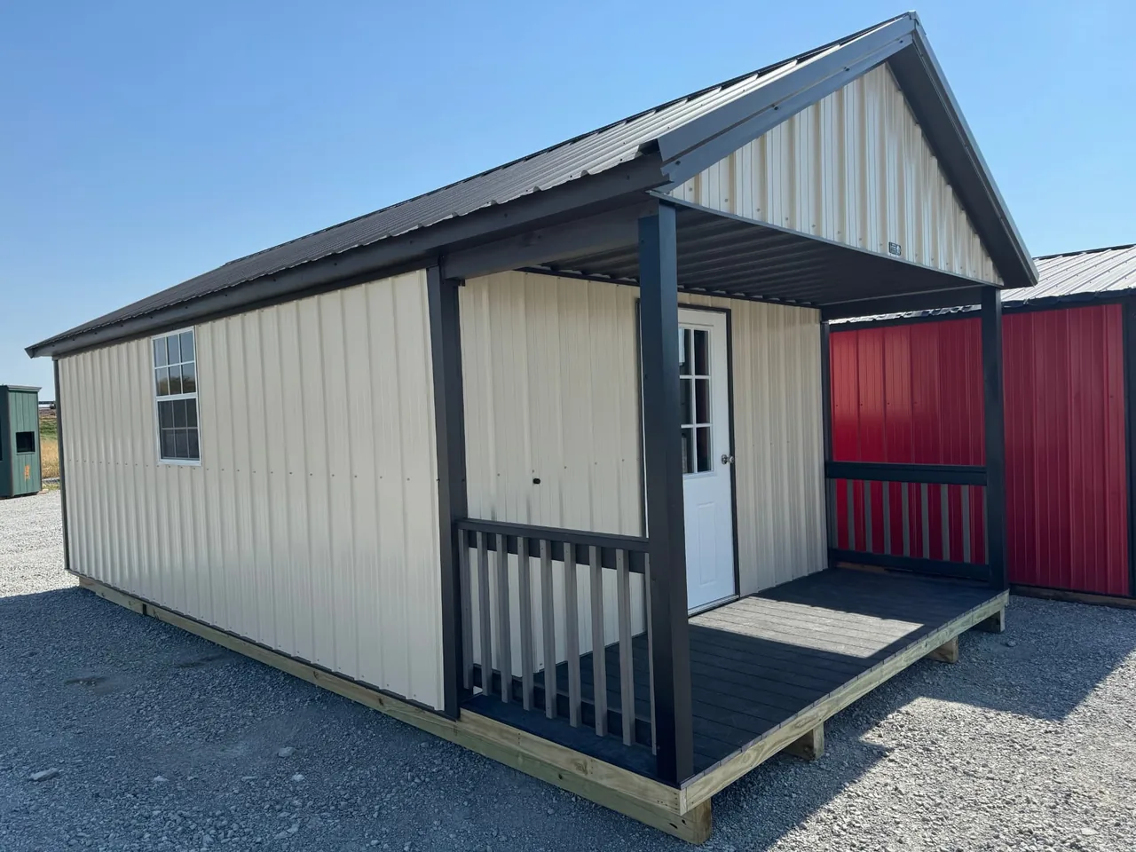 Angled view of cream-colored metal cabin with black roof, side window, and covered front porch
