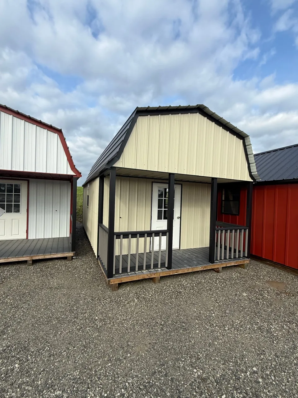 Cream-colored metal barn-style cabin with dark gambrel roof, black trim, and front porch